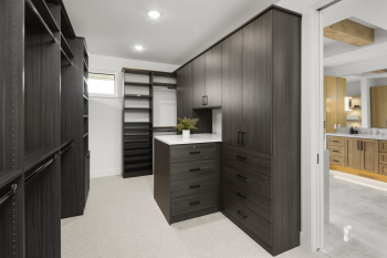 Dark Grey wood grain walk-in closet with small island that has drawers and light accent stone countertop