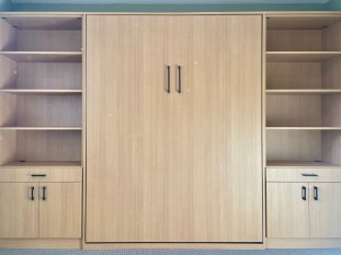 Penpine finish all wall bed queen with lower cabinets and upper adjustable shelving. Wall bed opens with a window behind it.