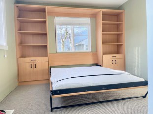Penpine finish all wall bed queen with lower cabinets and upper adjustable shelving. Wall bed opens with a window behind it.