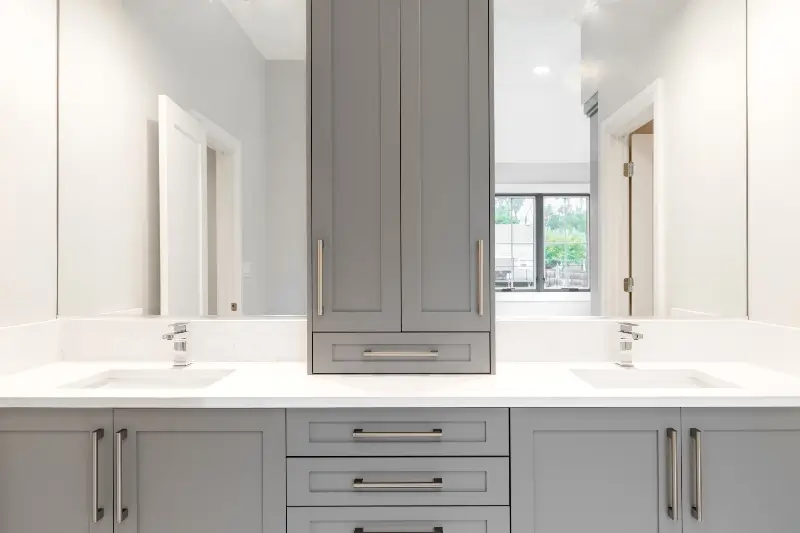 A gray vanity in a large luxurious bathroom with granite countertops and chrome fixtures