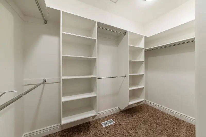 Interior of an empty walk-in closet with custom storage and a floor vent