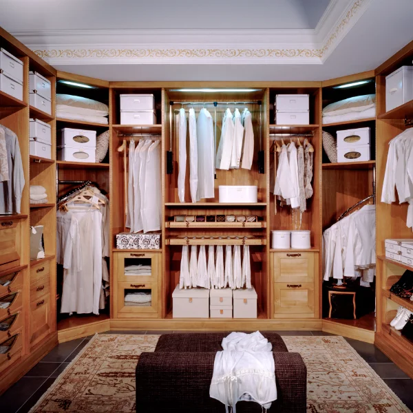 Large custom walk-in closet built with light wood cabinetry, featuring illuminated hanging racks, shelves, drawers, and shoe storage.