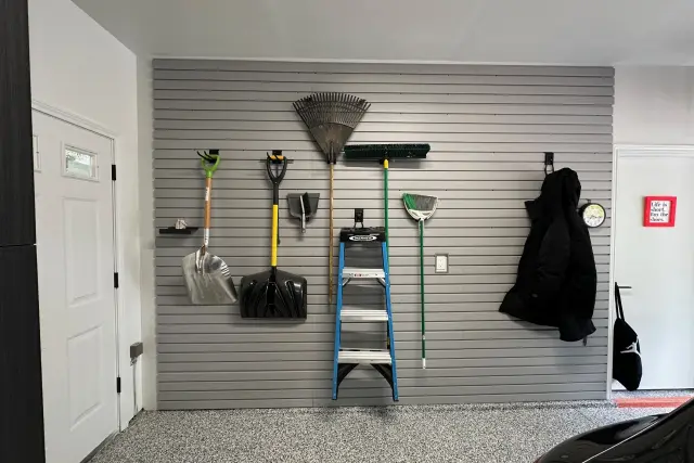 Grey slatwall garage organization system installed by Portland Closet Company with lawn tools and step ladder.