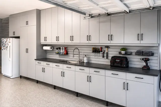Custom light grey garage cabinet system featuring built-in sink, slatwall backsplash, and EV charger setup in Portland, OR.