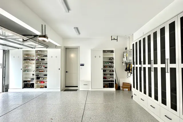 Custom white garage organization system featuring built-in shoe shelves and large glass-front cabinets by Portland Closet Company.